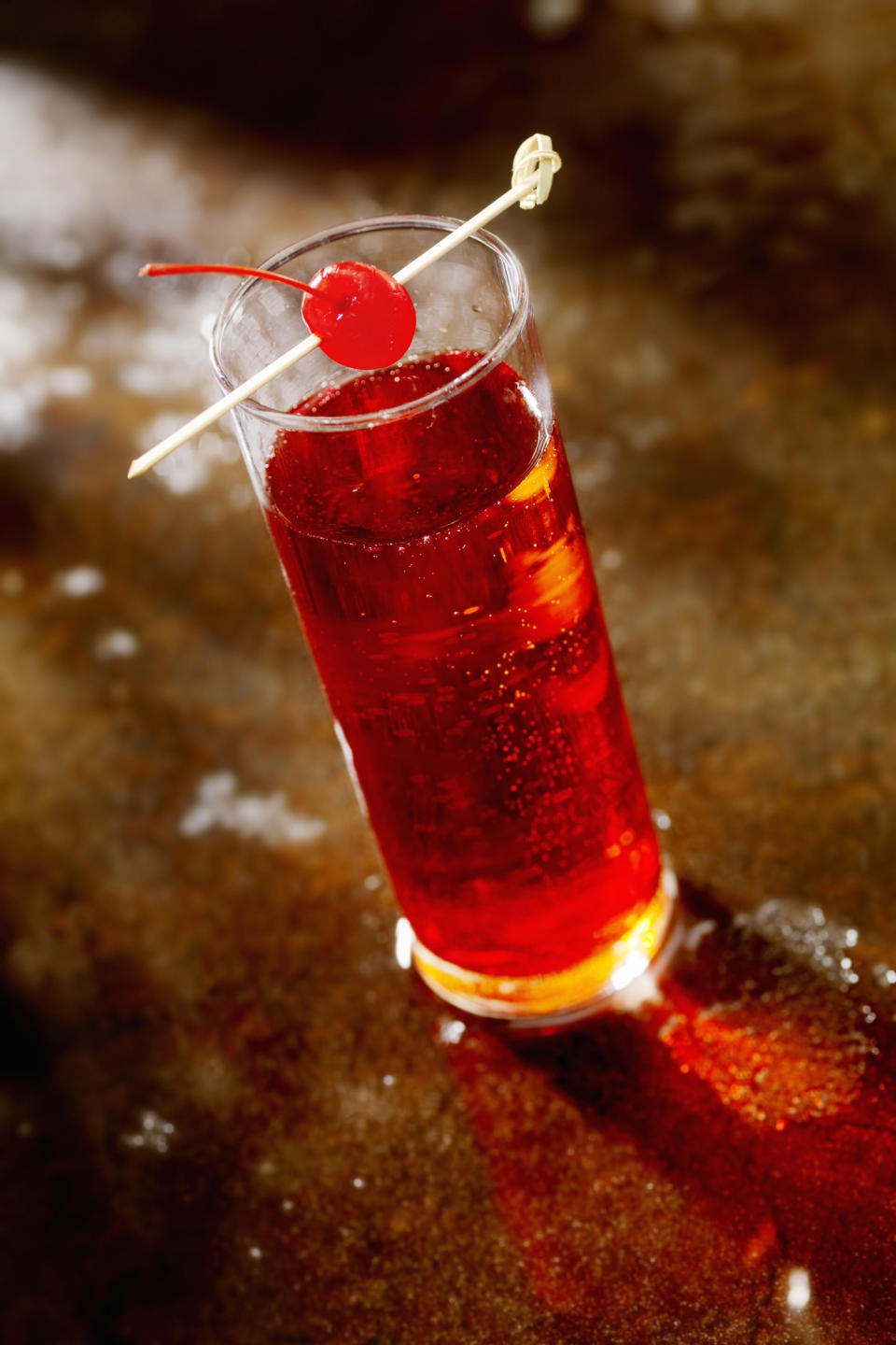 A glass of a drink with a cherry suspended above it on a toothpick