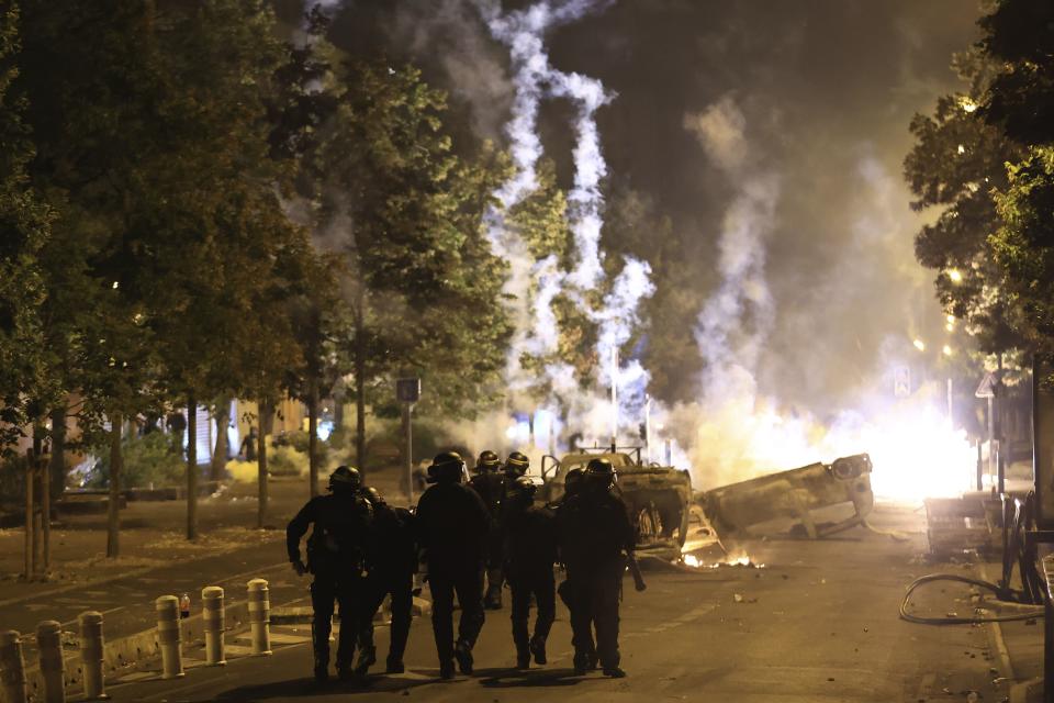 Riot police officers patrol as smoke billows from burnt vehicles on the third night of protests sparked by the fatal police shooting of a 17-year-old driver in the Paris suburb of Nanterre, France, Friday, June 30, 2023. The June 27 shooting of the teen, identified as Nahel, triggered urban violence and stirred up tensions between police and young people in housing projects and other neighborhoods. | Aurelien Morissard, Associated Press