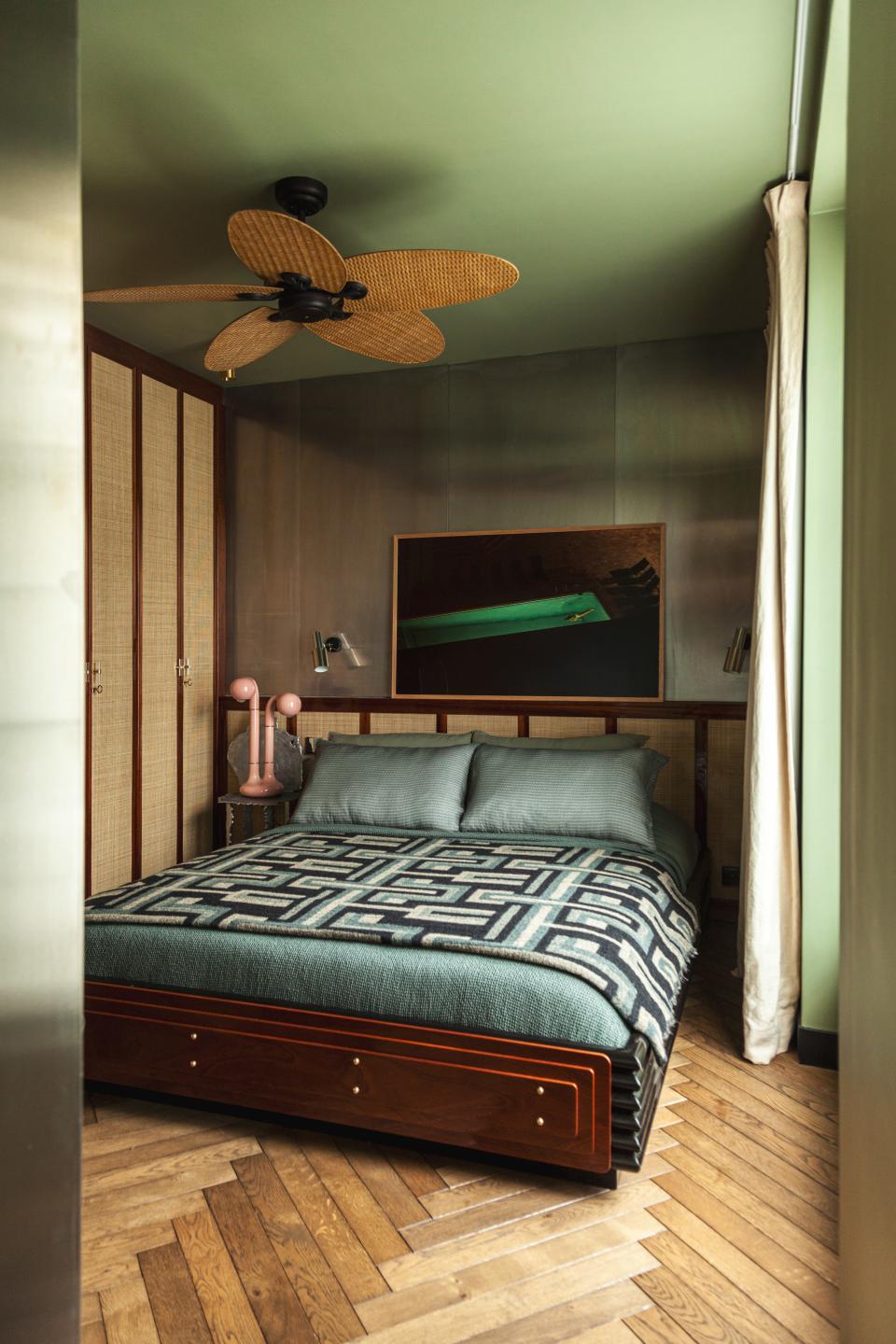 In the bedroom, painted in Lichen green by Farrow & Ball, Hugo Toro designed the bed. The Alualéatoure chair by Hélène de Saint Lager is used as a nightstand with a pink ceramic lamp by Entler Studio. The photo is by Clément Jolin, the curtains are by Silva Créations, and the bedding is by Society Limonta.