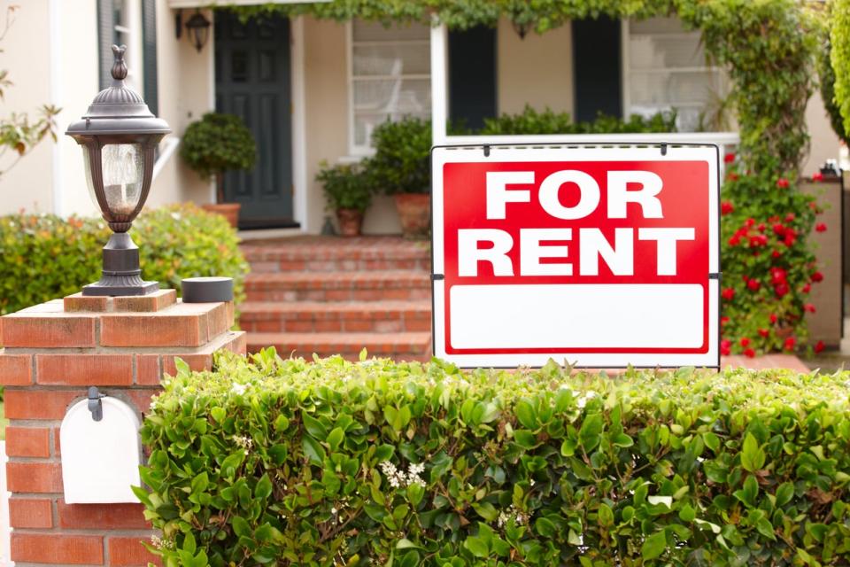 red for rent sign on front porch of stately home with shrubs and red flowers