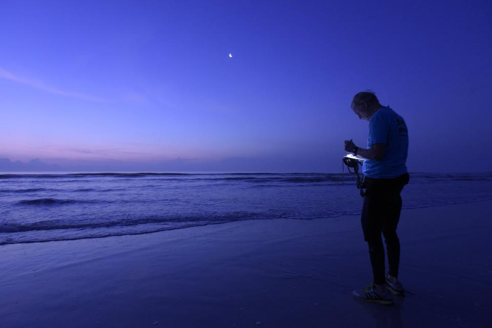 Bill Longenecker uses a small flashlight to read the thermometer he threw into the surf to check the water temperature for his morning surf report in this 2015 file photo.