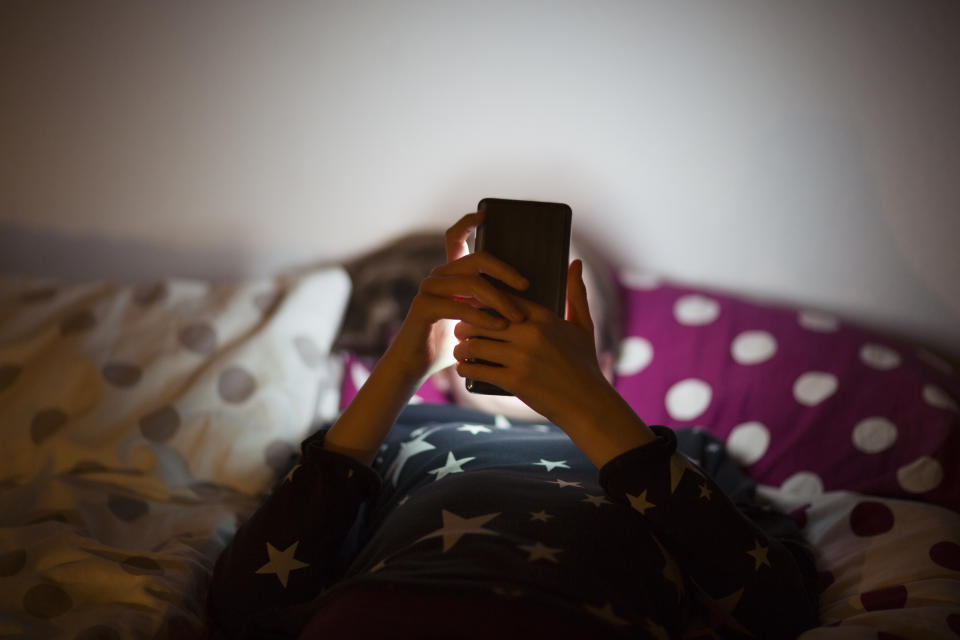little girl lying in bed on a phone for concussion recovery