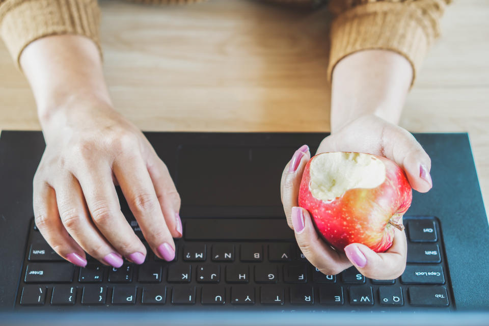 Woman hand working on computer and eating apple at desk for diet