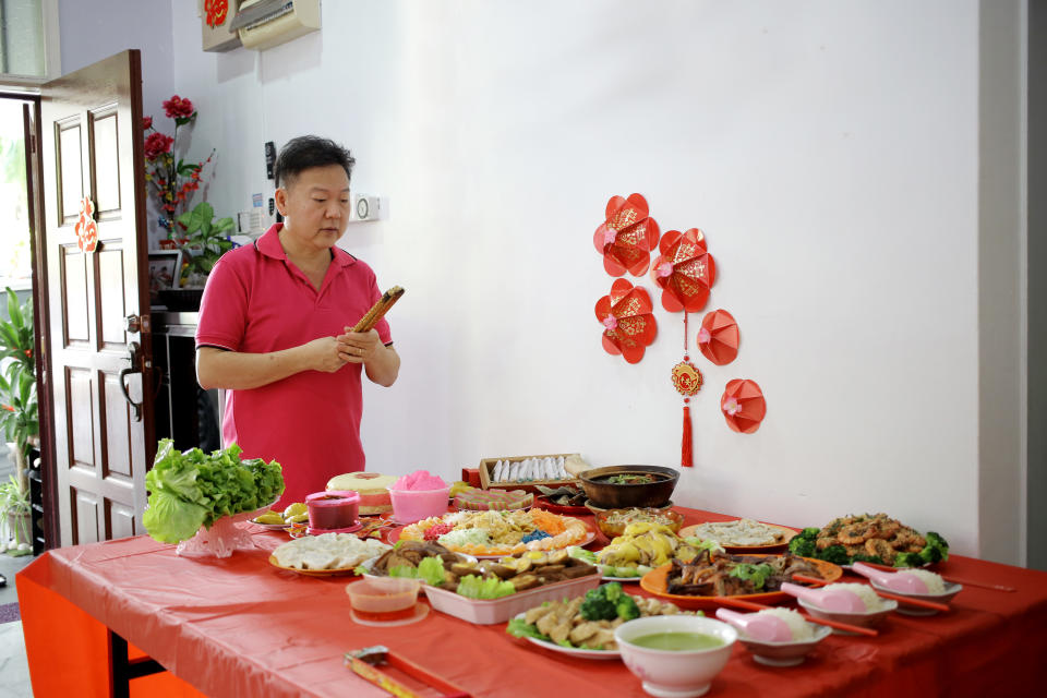 An Asian senior man praying with Chinese New Year offerings and prayers.