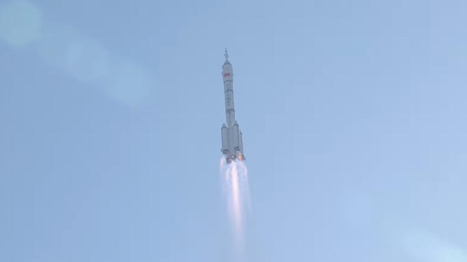 a white rocket rises into a blue sky.