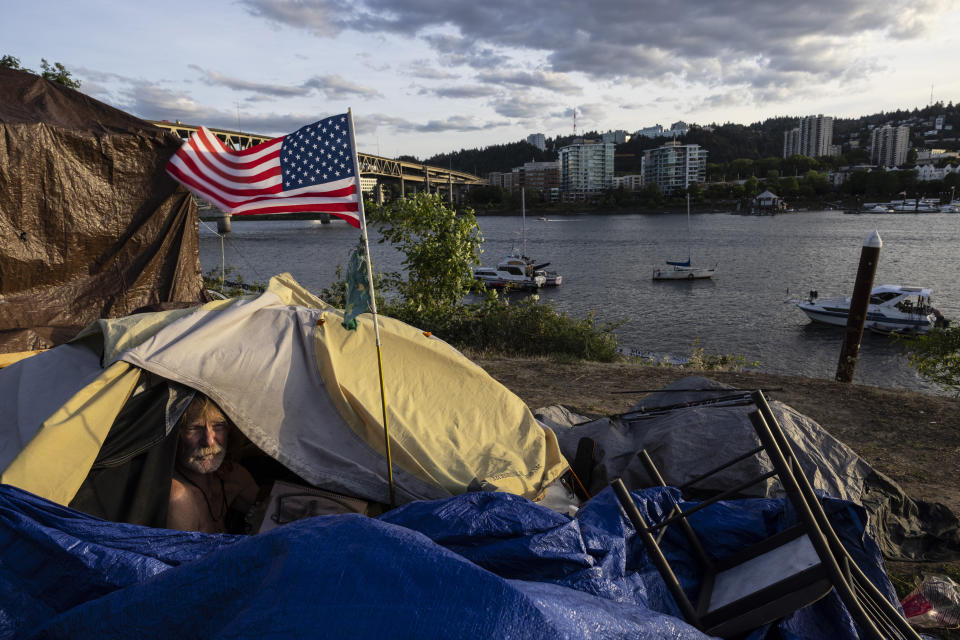 FILE - Frank, a homeless man sits in his tent with a river view in Portland, Ore., on June 5, 2021. The city of Portland will decide Wednesday, May 31, 2023, whether to ban homeless camping during daytime hours in most public places. Portland City Council will vote on a measure that would prohibit camping between 8 a.m. and 8 p.m. in city parks and near schools and day cares. (AP Photo/Paula Bronstein, File)