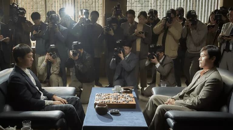 two men play a chess match as a crowd watches