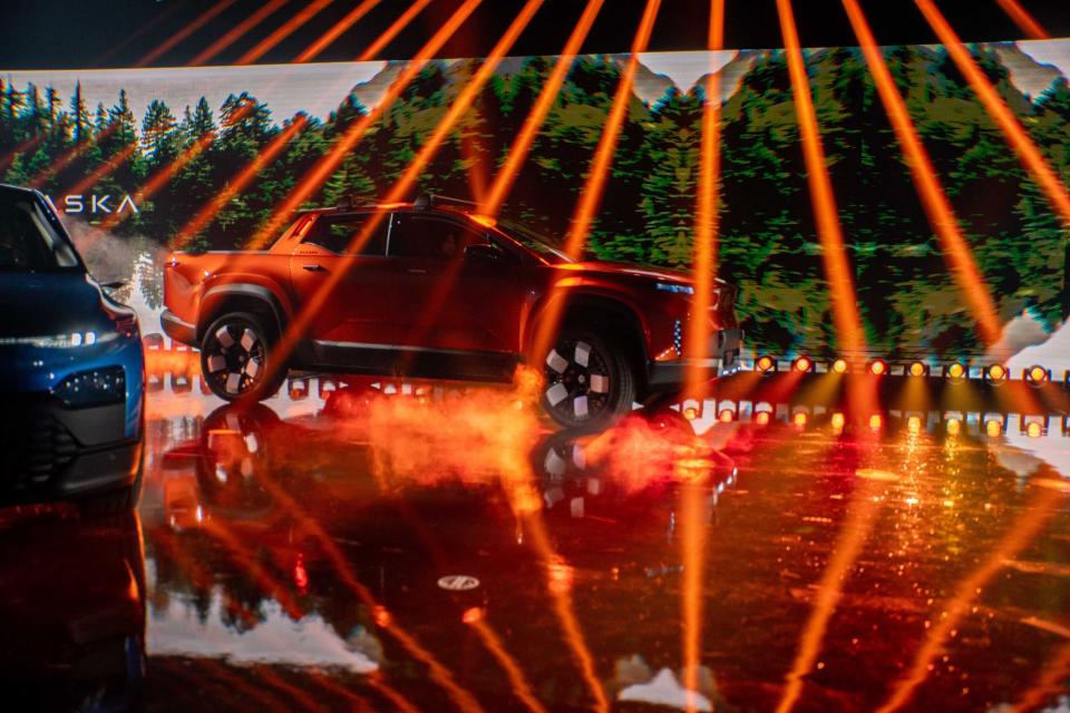 The orange Fisker Alaska electric pickup truck, on stage at an event.