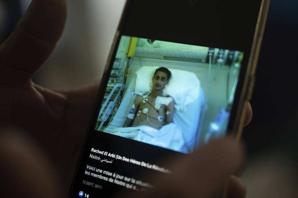 The mother of Rached El Arbi, a protester who was paralyzed after being shot during Tunisia's democratic uprising 10 years ago, holds a photo of her son on a mobile phone, in Tunis, Tunisia, Tuesday, Jan. 12, 2021. Rached El Arbi, now 30, has been paralyzed since being shot while protesting the autocratic regime of Tunisia's President Zine El Abidine Ben Ali, who was overthrown on Jan. 14, 2011. A photo of El Arbi hospitalized at the time went viral across the Arab world. (AP Photo/Mosa'ab Elshamy)