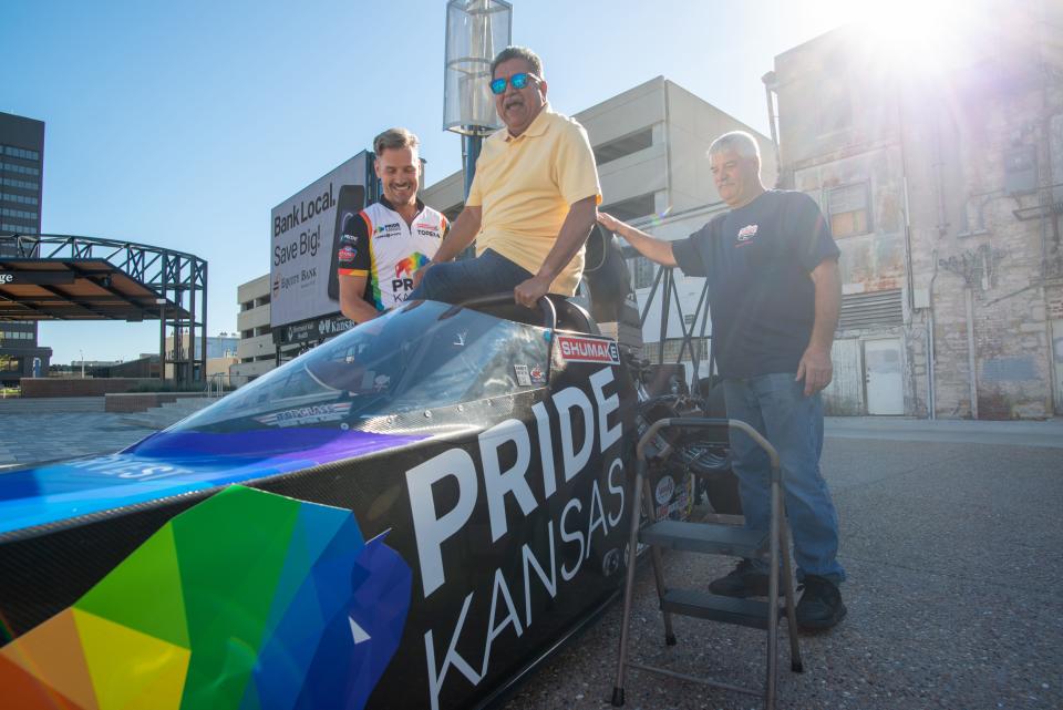 Topeka mayor Mike Padilla, middle, his helped in to the cockpit of a drag car that will be driven by Travis Shumake, left, this weekend at Heartland Park Speedway during a media event Wednesday morning at Evergy Plaza.