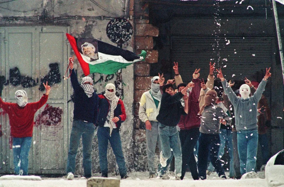 Masked Hamas terrorists stand in front of a mural of assassinated Hamas leaders Sheikh Ahmed Yassin and Abdel Aziz al-Rantissi.