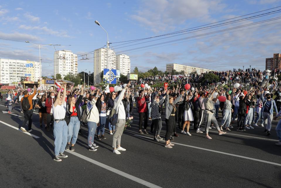 People with flowers and old Belarusian national flags shout slogan "Go away!" as they gather to protest against the results of the country's presidential election in Minsk, Belarus, Thursday, Aug. 13, 2020. Crowds of protesters in Belarus swarmed the streets and thousands of workers rallied outside industrial plants to denounce a police crackdown on demonstrations over a disputed election that extended the 26-year rule of authoritarian President Alexander Lukashenko. (AP Photo/Sergei Grits)