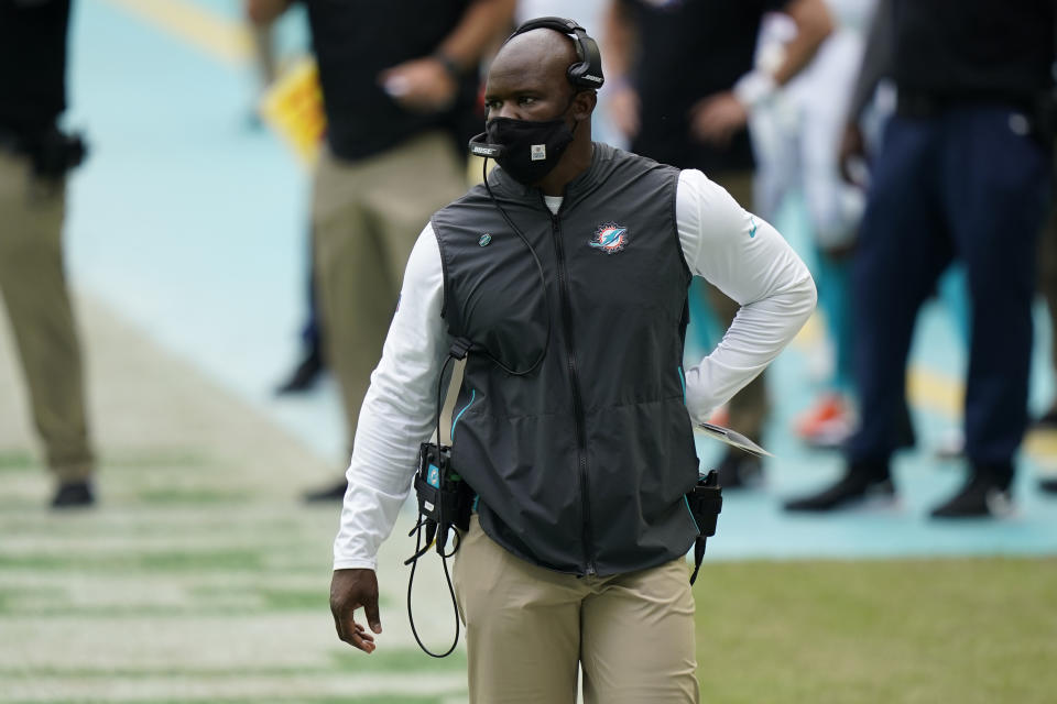 Brian Flores, wearing a mask and a headset, walks the sideline during a game.