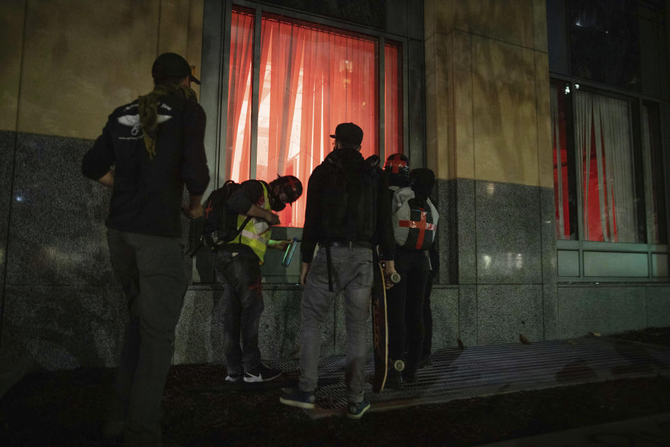 Protesters watch a flare inside of a federal building during a protest on Saturday, July 25, 2020, in Oakland, Calif. Protesters in California set fire to a courthouse, damaged a police station and assaulted officers after a peaceful demonstration intensified late Saturday, Oakland police said. (AP Photo/Christian Monterrosa)