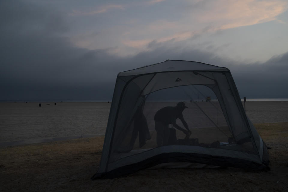 Marc Dilk, a 32-year-old homeless man, tidies up around his tent on the beach in the Venice neighborhood of Los Angeles, Tuesday, June 29, 2021. (AP Photo/Jae C. Hong)