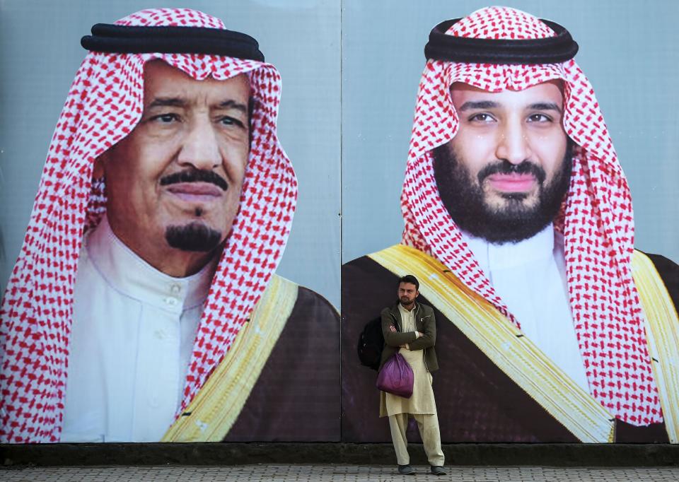 A Pakistani man waits for transport in front of billboards showing portraits of Saudi Arabian Crown Prince Mohammed bin Salman (R) and his father and Saudi Arabia's King Salman bin Abdulaziz displayed on a street ahead of the prince's arrival in Islamabad on February 15, 2019.