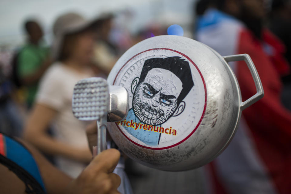 A demonstrator bangs on a pot that has a cartoon drawing of Governor Ricardo Rossello and text the reads in Spanish "Quit Ricky" as people gather to protest against Gov. Rossello, in San Juan, Puerto Rico, Friday, July 19, 2019. Protesters are demanding Rossello step down for his involvement in a private chat in which he used profanities to describe an ex-New York City councilwoman and a federal control board overseeing the island's finance. (AP Photo/ Dennis M. Rivera Pichardo)