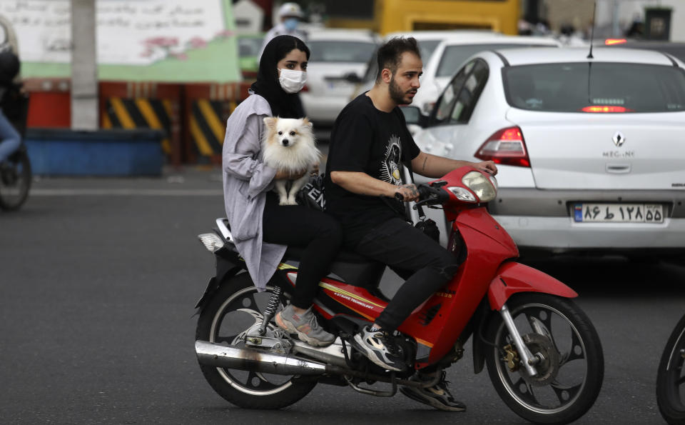 A woman holds a dog on a motorcycle while crossing an intersection in downtown Tehran, Iran, Tuesday, May 11, 2021. (AP Photo/Vahid Salemi)