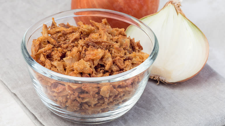 crispy onoins in a glass bowl on a cutting board next to a raw onion