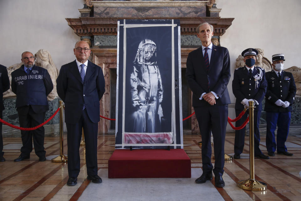 Franch Ambassador to Italy, Christian Masset, right, and Italian prosecutor Michele Renzo pose next to a recovered stolen artwork by British artist Banksy, depicting a young female figure with a mournful expression, that was painted as a tribute to the victims of the 2015 terror attacks at the Bataclan music hall in Paris, at the French Embassy in Rome, Tuesday, July 14, 2020. (AP Photo/Domenico Stinellis)