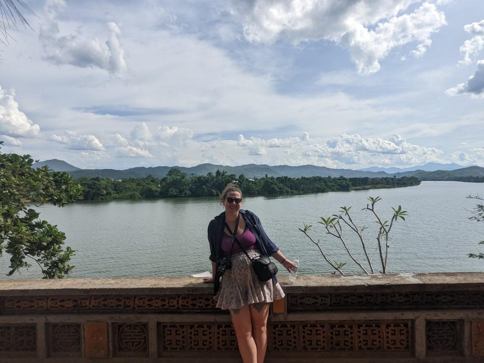 A woman poses for a picture on a bridge in front of a body of water.