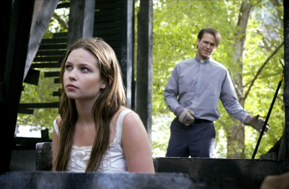 A young woman is approached by a priest while sitting in the remains of a decrepit building