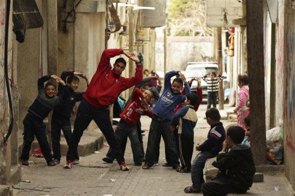 Gaza runner Bahaa al-Farra stretches during a training session as children mimic him while posing for the camera in Shati refugee camp in Gaza City, March 25, 2012.