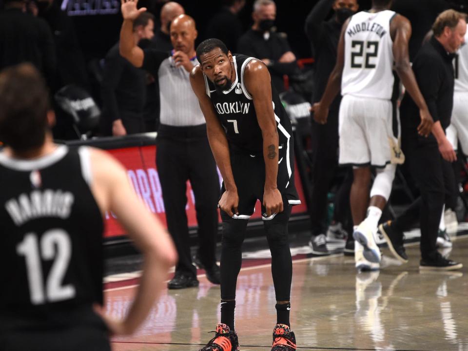Kevin Durant rests his hands on his knees and looks up as Nets and Bucks players walk off the court during a game.
