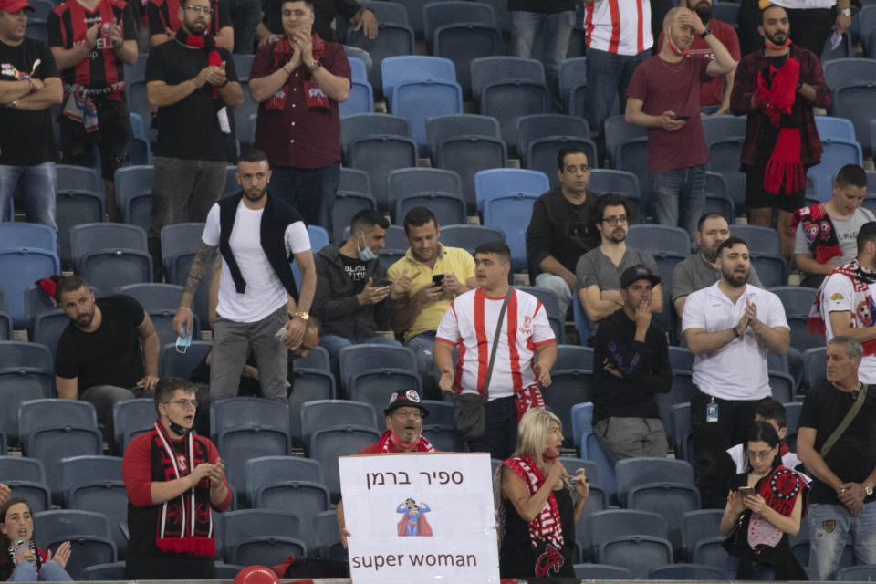 A fan holds a sign with the name of referee Sapir Berman during an Israeli Premier League soccer match between Hapoel Haifa and Beitar Jerusalem in the northern Israeli city of Haifa, Monday, May 3, 2021. Israeli soccer's first transgender soccer referee took the field Monday for the first time since coming out publicly as a woman last week. (AP Photo/Sebastian Scheiner)