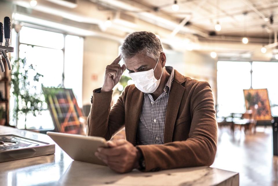 Mature businessman with mask using digital tablet at work.