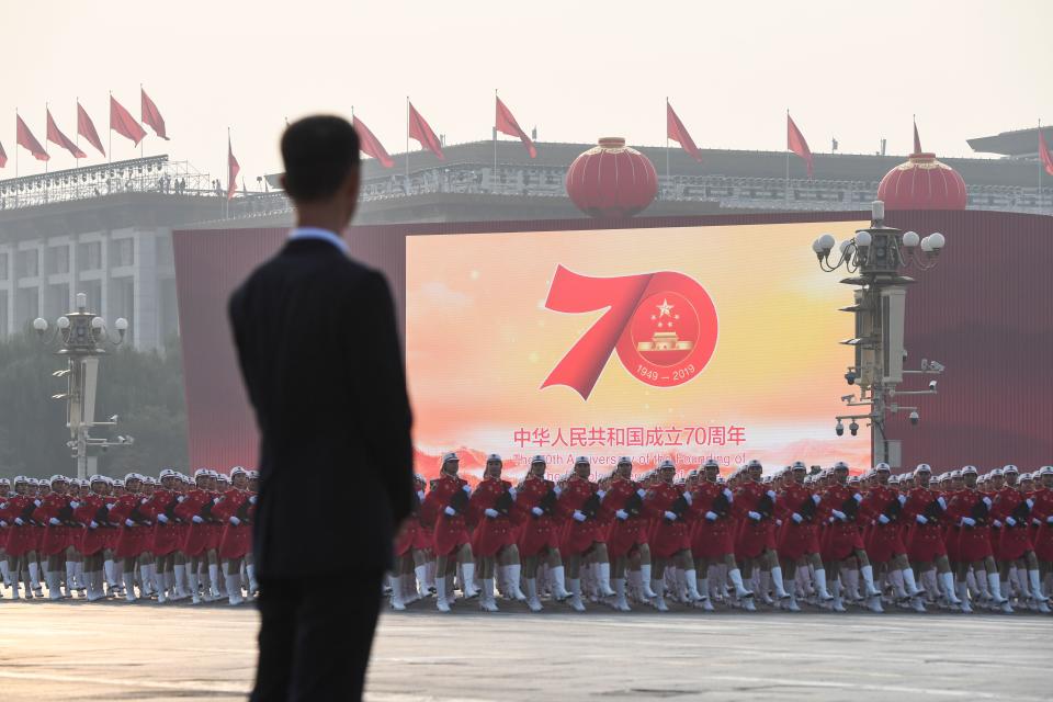 TOPSHOT - Chinese troops take part in a rehearsal in front of a screen shows the emblem of the 70th anniversary of the founding of the Peoples Republic of China ahead of a military parade in Tiananmen Square in Beijing on October 1, 2019. (Photo by GREG BAKER / AFP)        (Photo credit should read GREG BAKER/AFP/Getty Images)