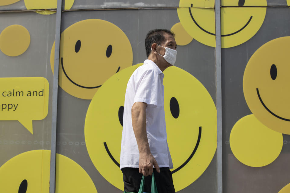 A resident wearing a mask to curb the spread of the coronavirus walks past smiley faces outside a mall in Beijing Thursday, July 16, 2020. China's economy rebounded from a painful contraction to grow by 3.2% over a year earlier in the latest quarter as anti-virus lockdowns were lifted and factories and stores reopened (AP Photo/Ng Han Guan)