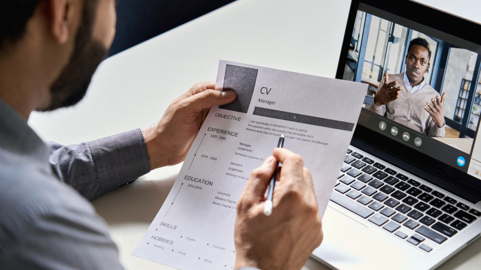 A person interviewing another man for a job virtually while he looks at his resume.