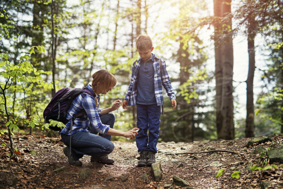 Mother and son hiking in forest. Mother is applying tick repellent on the son's legs.
Nikon D850