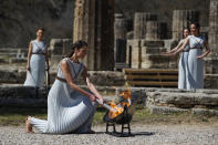 Greek actress Xanthi Georgiou, playing the role of the High Priestess, lights up the torch during the flame lighting ceremony at the closed Ancient Olympia site, birthplace of the ancient Olympics in southern Greece, Thursday, March 12, 2020. Greek Olympic officials are holding a pared-down flame-lighting ceremony for the Tokyo Games due to concerns over the spread of the coronavirus. Both Wednesday's dress rehearsal and Thursday's lighting ceremony are closed to the public, while organizers have slashed the number of officials from the International Olympic Committee and the Tokyo Organizing Committee, as well as journalists at the flame-lighting. (AP Photo/Thanassis Stavrakis)