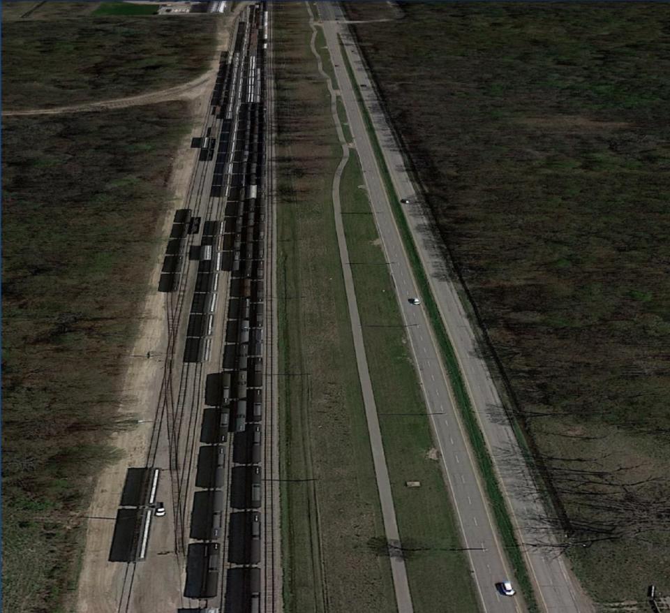 An aerial view of the four lanes of traffic on the Ojibway Parkway and the Essex Terminal Railway train tracks between Ojibway Park on the right and Black Oak Heritage Park on the left.