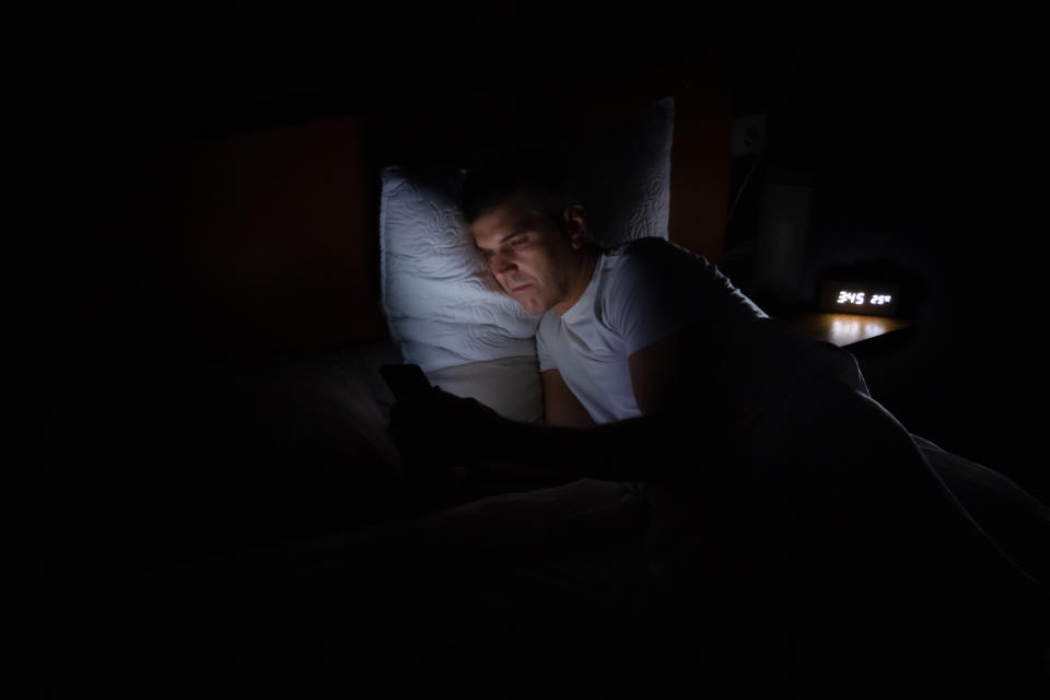 A man is lying in bed in total darkness looking at his smart phone. Lifestyle concept