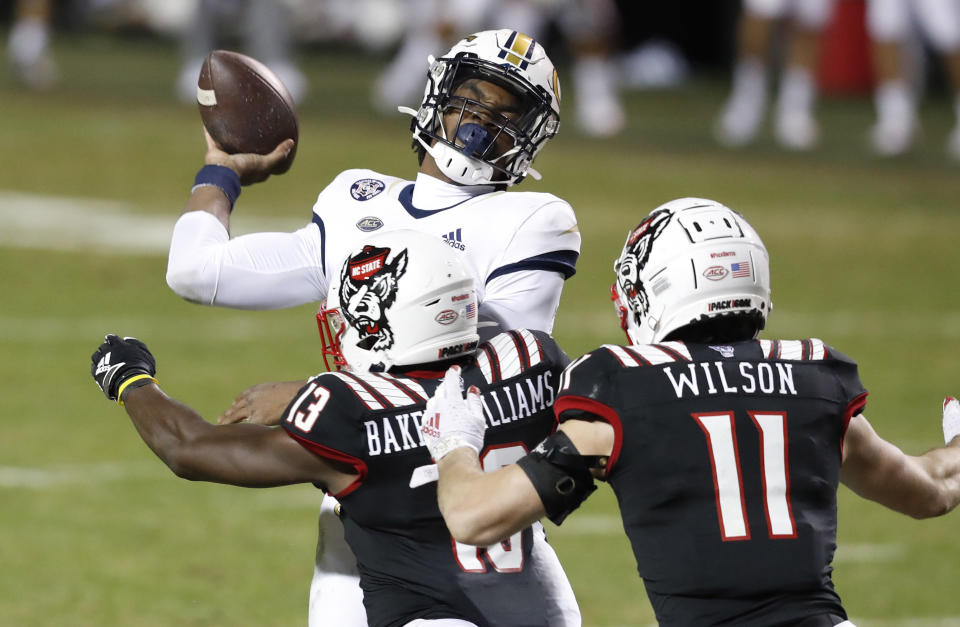 Georgia Tech quarterback Jeff Sims (10) throws as he is hit by North Carolina State defensive back Tyler Baker-Williams (13) during the first half of an NCAA college football game in Raleigh, N.C., Saturday, Dec. 5, 2020. N.C. State's Payton Wilson is at right (Ethan Hyman/The News & Observer via AP, Pool)