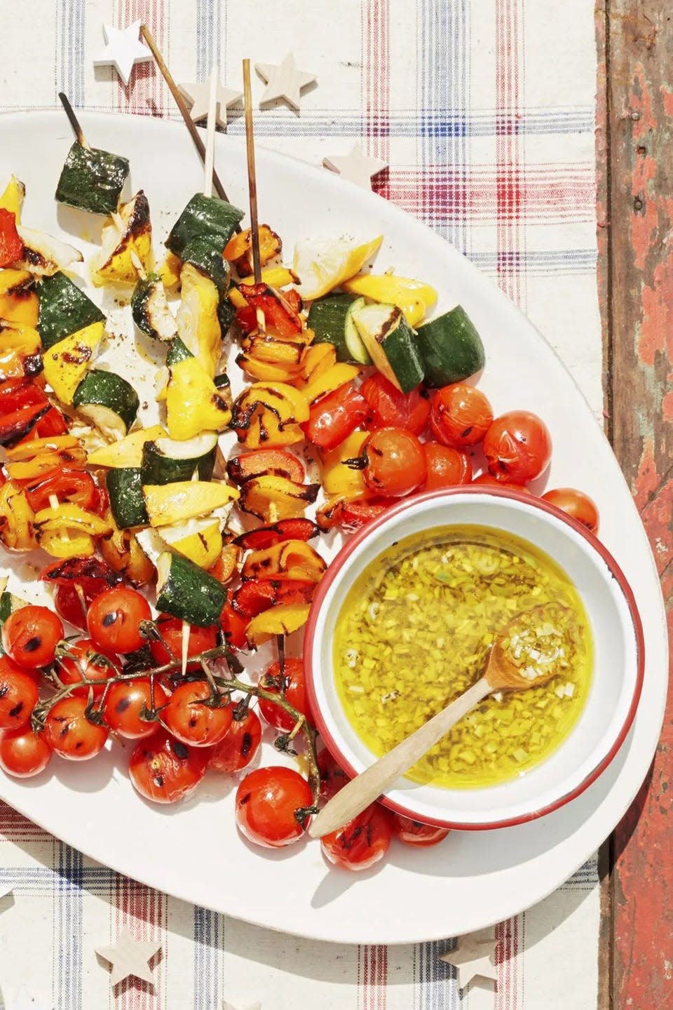 cherry tomato pepper and summer squash kebabs on a tray with a small bowl of lemon scallion vinaigrette