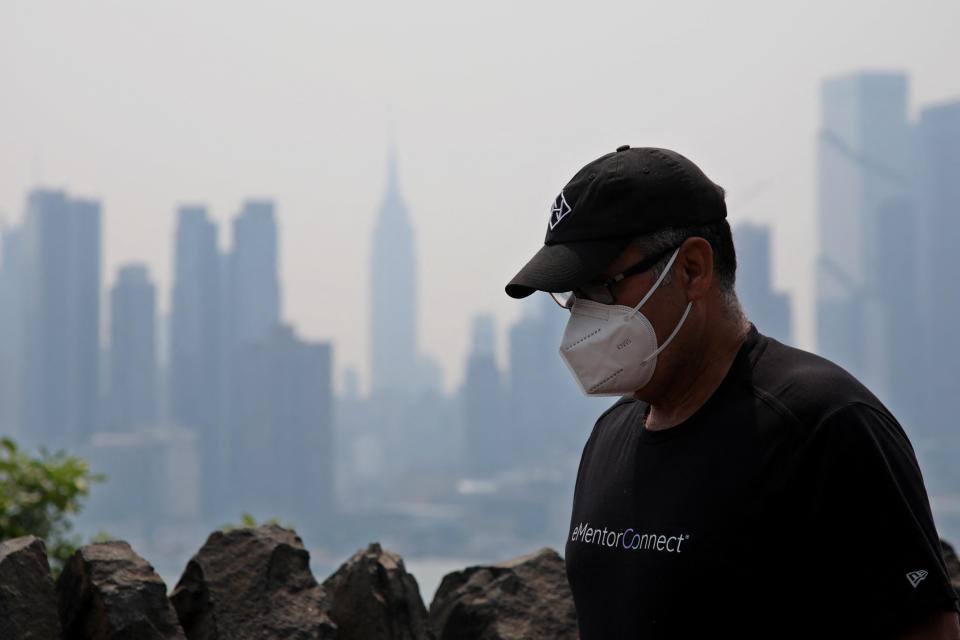 A man wearing a mask and baseball cap against the shrouded Manhattan skyline.
