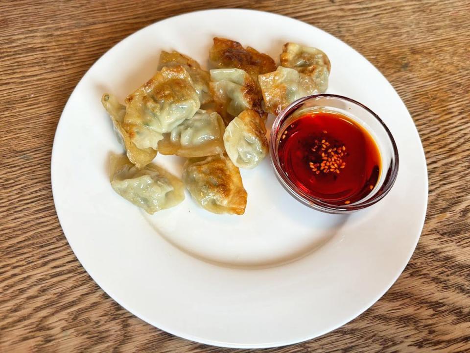 A white plate with golden-brown dumplings and a red-brown dipping sauce in a small bowl