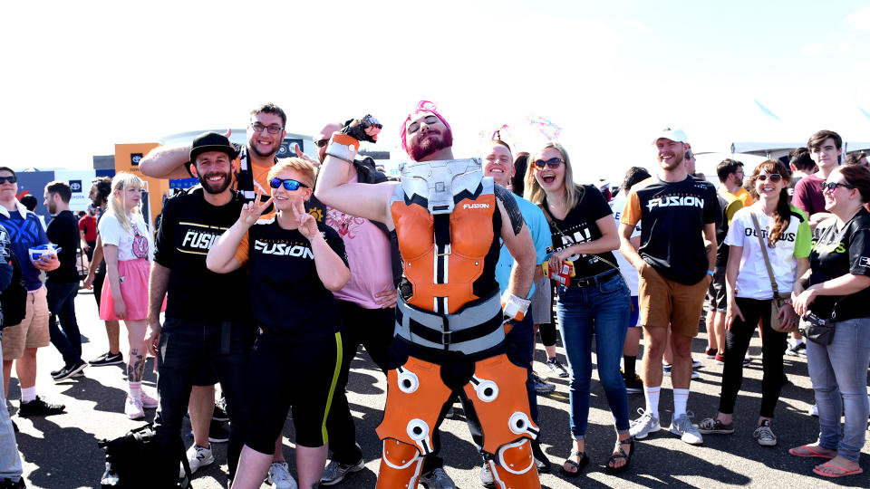 Fans stand outside the venue for the 2019 OWL Grand Finals, some wearing Philadelphia Fusion shirts. A Zarya cosplayer stands in the center.