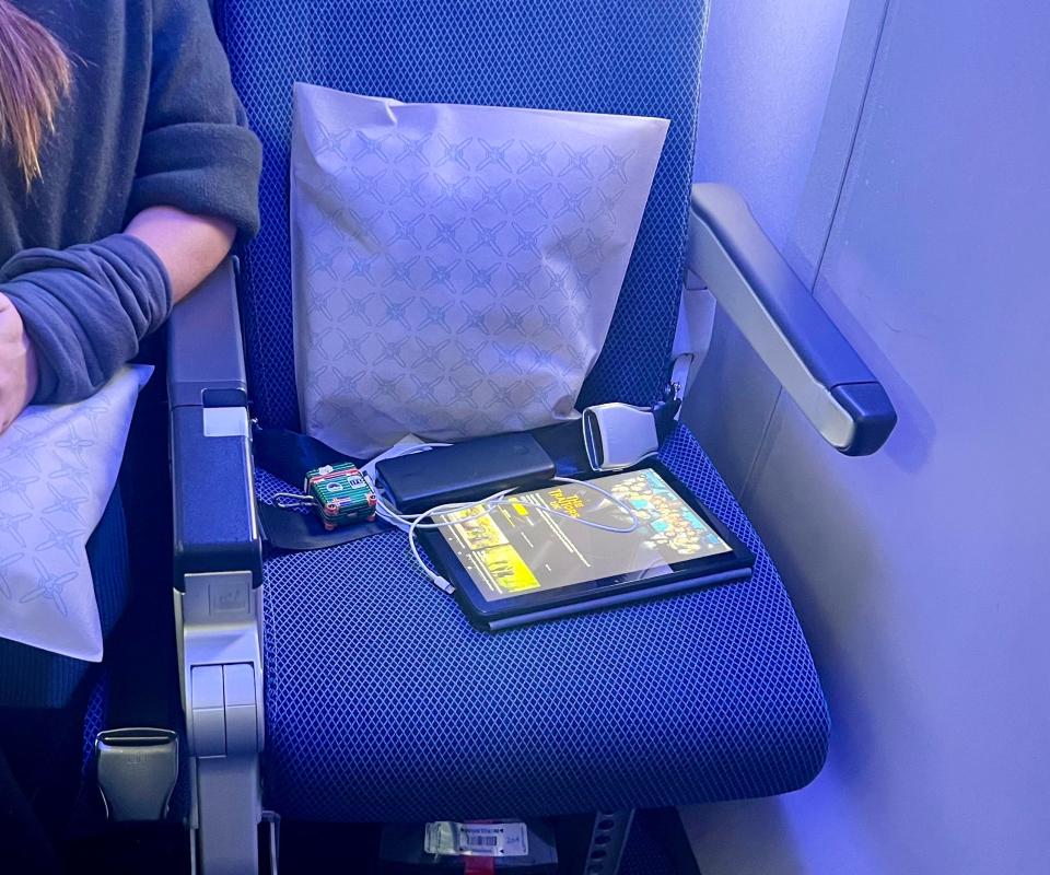 The economy seat with the author's Kindle, portable charge, and headphones on it.