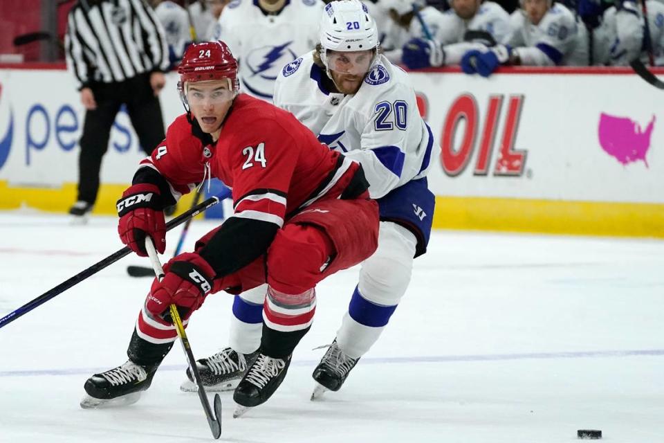Carolina Hurricanes defenseman Jake Bean (24) and Tampa Bay Lightning center Blake Coleman (20) chase the puck during the first period of an NHL hockey game in Raleigh, N.C., Monday, Feb. 22, 2021. (AP Photo/Gerry Broome)
