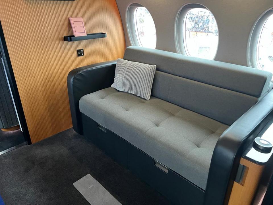 A couch onboard a Falcon 10X, with wood panel walls and three windows behind.