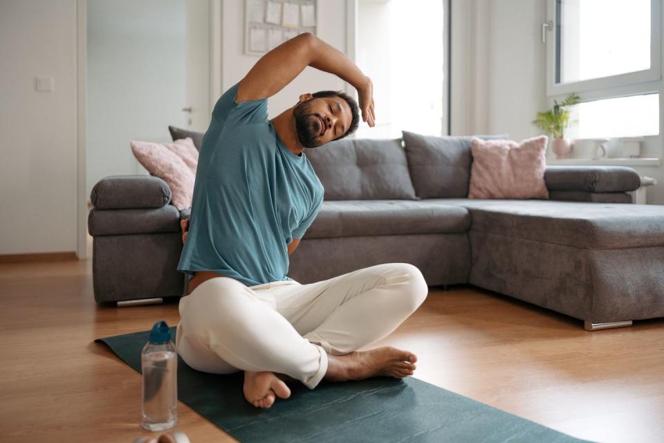 the single man exercising alone at home, stretching his back and arm young man is happy, relaxed, and content with his life solo home workout and meditation, morning or evening workout routine