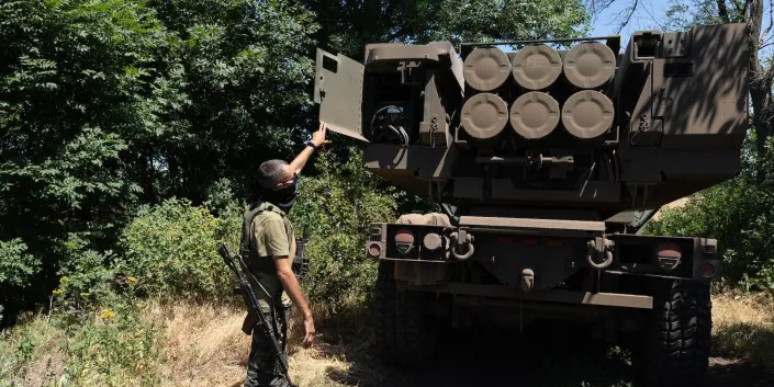 A Ukrainian solider shows the rockets on a HIMARS vehicle between some trees
