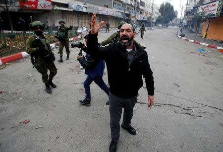 A Palestinian demonstrator gestures as Israeli soldiers are seen during a protest against U.S. President Donald Trump's decision to recognise Jerusalem as the capital of Israel, in the West Bank city of Hebron, December 29, 2017. REUTERS/Mussa Qawasma