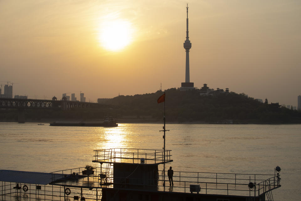 In this April 8, 2020, photo, a man looks across the Yangtze River as the sun sets in Wuhan in central China's Hubei province. The reopening of ferry service on the Yangtze River, the heart of life in Wuhan for more than 20 centuries, was an important symbolic step in official efforts to get business and daily life in this central Chinese city of 11 million people back to normal after a 76-day quarantine ended in the city at the center of the coronavirus pandemic. (AP Photo/Ng Han Guan)