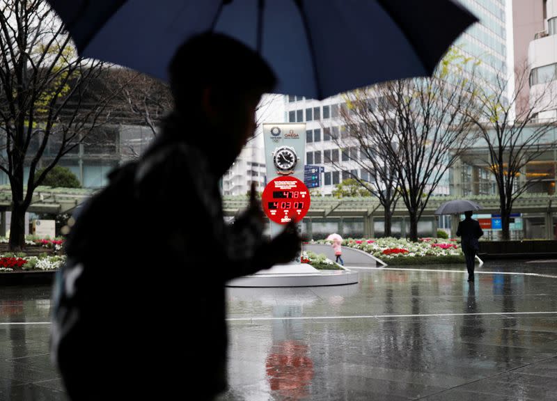 Passersby holding umbrellas walk past next to a countdown clock showing the adjusted days and time for the start of the postponed Tokyo Olympic Games, following an outbreak of the coronavirus disease (COVID-19) in Tokyo